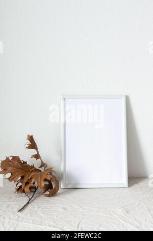 Casa decoratore moccap, quadro vuoto cornice vicino bianco dipinto muro di cemento, rami con foglie asciutte Foto Stock