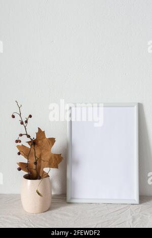 Casa decoratore moccap, quadro vuoto cornice vicino bianco dipinto muro di cemento, rami con foglie asciutte Foto Stock