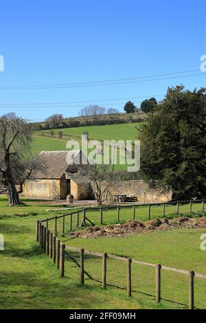 Il Cotswolds - scena di campagna con fienile, recinzioni e un trattore rosso in lontananza Foto Stock