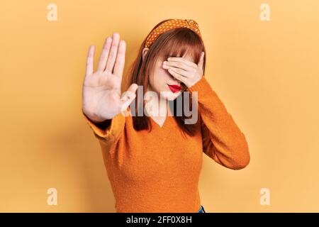 Giovane donna rossa indossando un maglione arancione casual che copre gli occhi con le mani e fa il gesto di stop con espressione triste e paura. Imbarazzata e negata Foto Stock