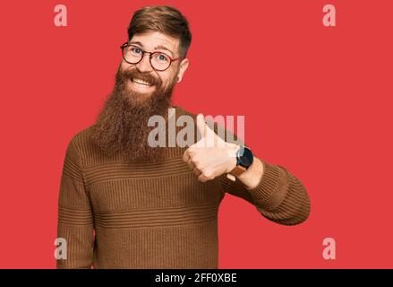 Giovane irlandese rosso uomo che indossa abiti casual e bicchieri facendo felice pollice su gesto con la mano. Approvando espressione guardando la fotocamera mostrare Foto Stock