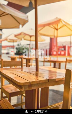 Terrazza sotto il tetto con tavoli e sedie in legno che si affaccia sul mare accanto alla piscina, tavolo e sedie in legno giallo e luce solare Foto Stock