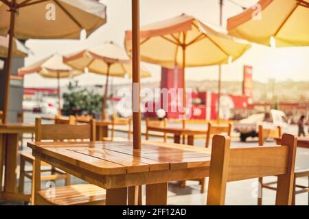Terrazza sotto il tetto con tavoli e sedie in legno che si affaccia sul mare accanto alla piscina, tavolo e sedie in legno giallo e luce solare Foto Stock
