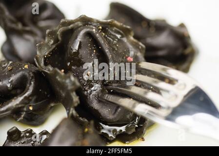 Agnolotti neri farciti di carne, un tipo di pasta tipica del Piemonte in Italia, primo piano con forchetta Foto Stock