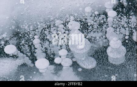 Lago Baikal congelato con crepe e bolle di metano sulla superficie trasparente del ghiaccio. Inverno astratto e sfondo di ghiaccio blu Foto Stock
