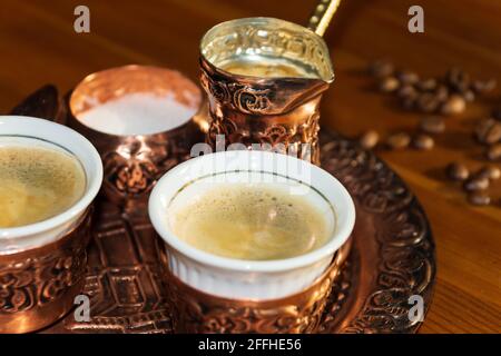 Caffè turco servito in una tazza di rame e caffè in grani su un tavolo di legno marrone. Foto Stock