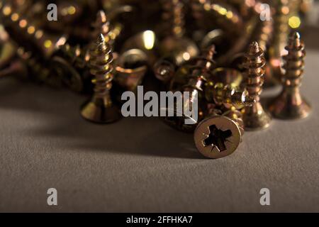 Immagine ravvicinata di un mucchio di viti per legno color oro su una superficie neutra, che enfatizza la struttura metallica e le teste delle viti Foto Stock