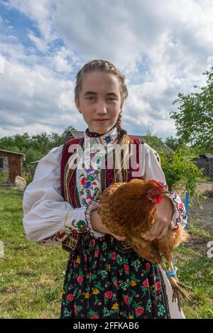 Salaj, Transilvania, Romania-14 maggio 2018: Bella giovane ragazza in costume tradizionale rumeno folk tenendo un pollo in una fiera di campagna a Marin Vill Foto Stock