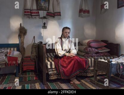 Salaj, Transilvania, Romania-14 maggio 2018: Bella giovane ragazza in costume tradizionale rumeno folk seduta all'interno di un'autentica casa contadina a Mari Foto Stock