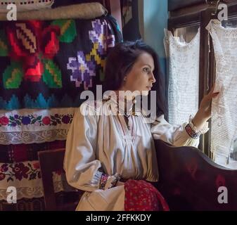 Salaj, Transilvania, Romania-14 maggio 2018: Bella giovane ragazza in costume tradizionale rumeno folk seduto alla finestra in un'autentica casa contadina Foto Stock