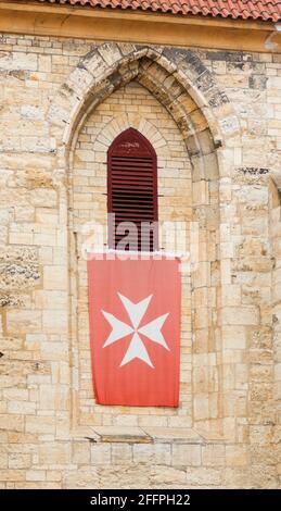 La bandiera del Sovrano Ordine ospedaliero militare di San Giovanni di Gerusalemme, di Rodi e di Malta sulle mura di un vecchio edificio storico. Foto Stock