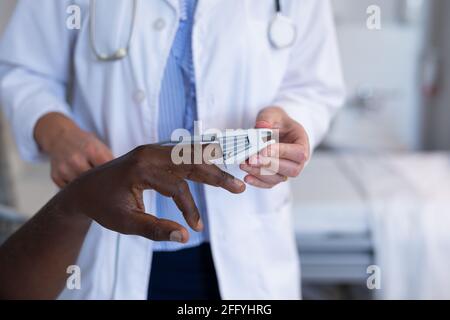 Midsection di diverse donne medico e paziente maschile attaccando polso ossimetro sul dito Foto Stock