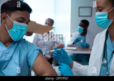 Razza mista coppia di medici che indossano maschere facciali facendo l'iniezione Foto Stock