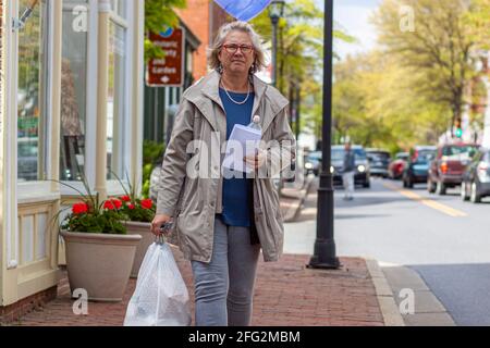 Easton, MD, USA 04-16-2021: Una donna anziana bionda sta trasportando un sacchetto pieno di cestino in sacchetti bianchi pesanti della spazzatura di servizio con la parte superiore schiacciata ed il manico. Cestino Foto Stock