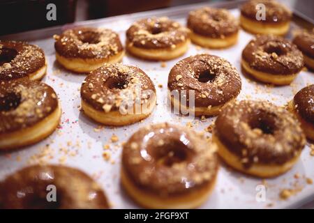 Deliziose ciambelle dall'aspetto irresistibile con condimento al cioccolato e biscotti schiacciati sulla parte superiore del vassoio in un laboratorio di caramelle. Pasticceria, dessert, sw Foto Stock