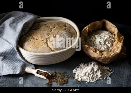 Pane di pasta acida che si innalza in un cesto di legno arrangiato con farina e cumino Foto Stock