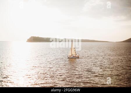 La barca a vela bianca naviga sul mare sullo sfondo della montagna. Il sole splende di luce Foto Stock