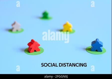 diverse piccole figure di legno multicolore di persone si trovano a distanza l'una dall'altra, su sfondo blu. testo sociale distansing ofl font. concep Foto Stock