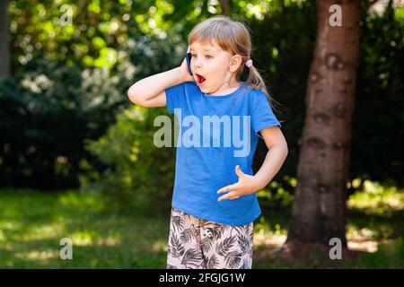 Bambino felice, ragazza che parla sul telefono cellulare, tenendo il suo smartphone accanto al suo orecchio molto sorpreso, wow espressione del volto, reagendo a emozionante Foto Stock