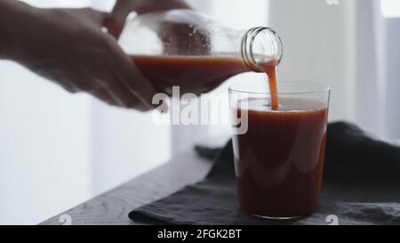 l'uomo versa il succo di pomodoro in un bicchiere da bicchiere su un panno di lino, foto ampia Foto Stock