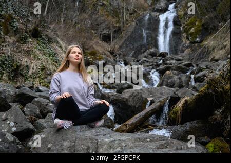 La ragazza si siede su un albero e medita vicino al fiume di montagna In Abkhazia Foto Stock