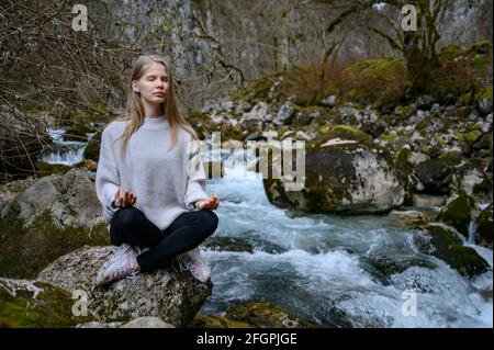 La ragazza si siede su un albero e medita vicino al fiume di montagna In Abkhazia Foto Stock
