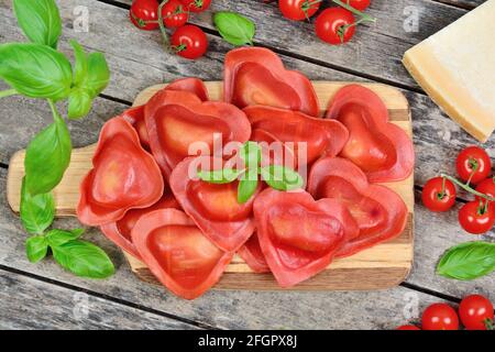 Ravioli a cuore rosso con pomodoro, mozzarella e basilico su sfondo ligneo Foto Stock