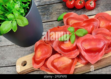 Primo piano di ravioli a cuore rosso con pomodoro, mozzarella e basilico su sfondo ligneo Foto Stock