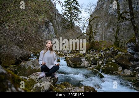La ragazza si siede su un albero e medita vicino al fiume di montagna In Abkhazia Foto Stock