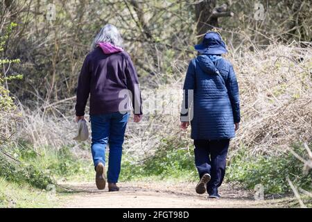 Donne anziane che camminano nel Regno Unito; due donne anziane che camminano in campagna, viste dal retro, in primavera, Lackford Lakes, Suffolk UK Foto Stock