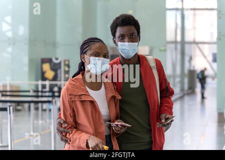 Ritratto di felice coppia nera in maschere con carte d'imbarco e passaporti in aeroporto in covid-19 Foto Stock