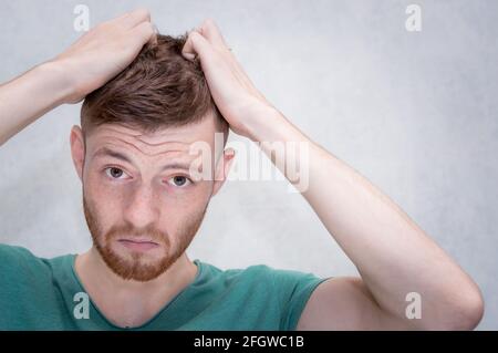 Il giovane strappa i capelli sulla testa per fastidio. Ritratto di primo piano Foto Stock