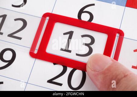 Un dito che punta al tredicesimo giorno del mese su un calendario. Primo piano. Foto Stock
