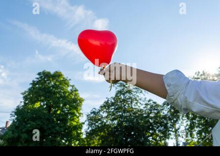 Una mano che tiene un palloncino rosso a forma di cuore sullo sfondo del  cielo luminoso Foto stock - Alamy