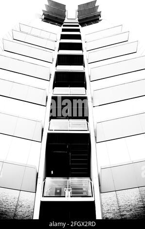 Un'immagine verticale in scala di grigi di un alto edificio moderno sotto con balconi e finestre di vetro Foto Stock