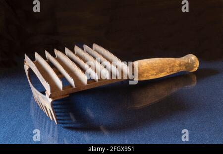 Un vecchio pettine animale sul tavolo con un riflesso. Utensile in ferro con manico in legno su sfondo nero Foto Stock