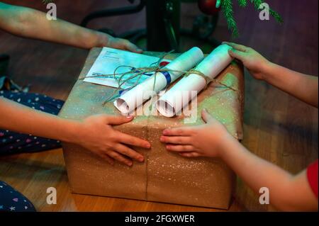 regalo avvolto sotto un albero di natale nelle mani dei bambini a casa. i capretti del fratello piccolo danno a vicenda i regali. scatola dei regali domestici di festa di nuovo anno wra Foto Stock