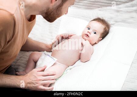 il giovane padre moderno si sta occupando del suo figlio neonato. Cambia il pannolino sul letto. Concetto di igiene e cura del neonato. Amore e cura del Padre. D. Del Padre Foto Stock