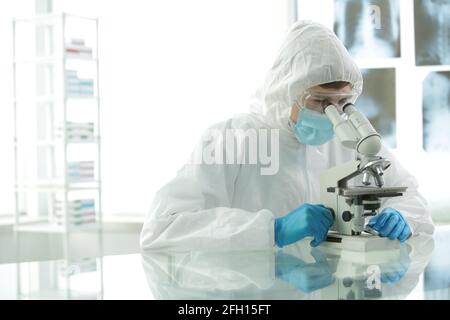 Medico in tuta protettiva che indossa una maschera blu i guanti in laboratorio si trovano al microscopio Foto Stock