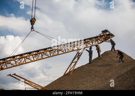 Impianti di estrazione e trasformazione. Addetti all'assemblaggio di macchine per frantumazione rocce. Utilizzare per la distruzione del minerale d'oro. Trave di sollevamento in metallo. Cielo blu, nuvole. Foto Stock