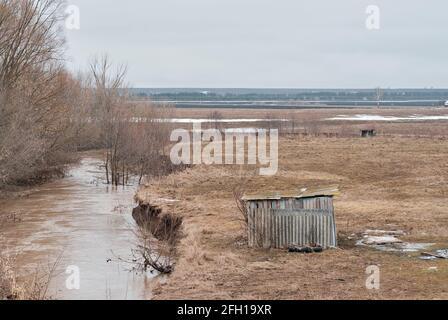 Vista dall'alto delle rovine delle case abbandonate in legno e del piccolo fiume nel villaggio fantasma nel Nord europeo della Russia. Vecchia capanna vicino al fiume, vista dall'alto Foto Stock