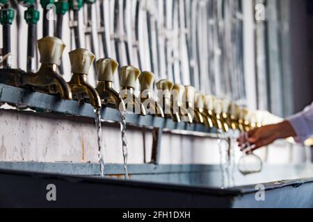 Stazione di purificazione dell'acqua.Pipes e rubinetti sovietici vintage (in fuoco a sinistra). Il chimico preleva il campione di acqua purificata in matraccio (fuori fuoco). Kyzylorda, KZ. Foto Stock