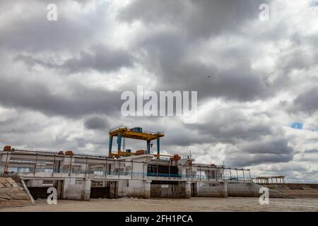 Diga del fiume Shardara vicino alla città di Kazaly. Gru a cavalletto sul ponte. Nuvole grigie e acqua gialla. Regione di Kyzylorda, Kazakistan Foto Stock