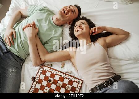 Felice giovane coppia sta posando e baciando a letto con scacchi su di esso. Giovane famiglia che si sposta in un nuovo appartamento Foto Stock
