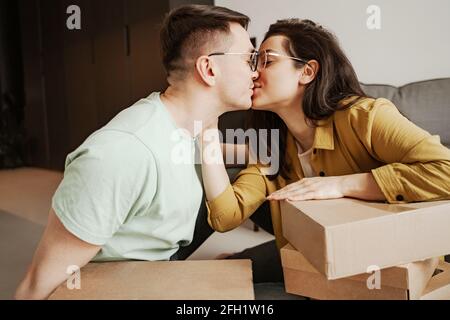 La coppia felice sta baciando sedendosi sulla farina con le scatole a casa. Giovane famiglia che si sposta in un nuovo appartamento Foto Stock