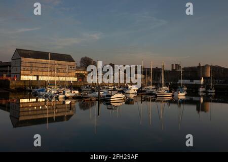 Barche ormeggiate a Victoria Dock, Caernarfon, Galles alla luce del sole serale. Castello e mura cittadine sullo sfondo Foto Stock