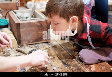 Primo piano di un uomo fabbro che tiene in mano una padella di metallo con un piombo fuso nel laboratorio, top view.Iron e acciaio industria. Fusione di stagno in un WO Foto Stock