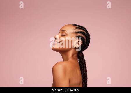Vista laterale di un modello femminile con pelle sana e impeccabile. Donna afroamericana con acconciatura intrecciata su sfondo rosa. Foto Stock