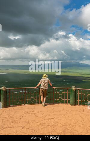 Vista verticale da un uomo si affaccia sulla zona di conservazione di Ngorongoro con il lago Magadi dal punto di vista, Tanzania, vista con cielo drammatico Foto Stock