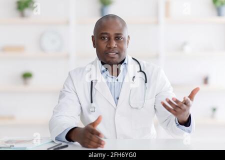 Il punto di vista del paziente sulla consultazione medica. Nero maschio medico gesturing a macchina fotografica nel suo ufficio Foto Stock